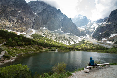 Rear view of person sitting on rock by lake