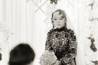 Portrait of bride holding bouquet standing against wall