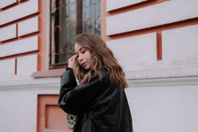 Young woman looking away while standing against brick wall