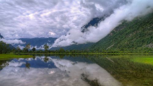 Scenic view of lake by mountains against cloudy sky