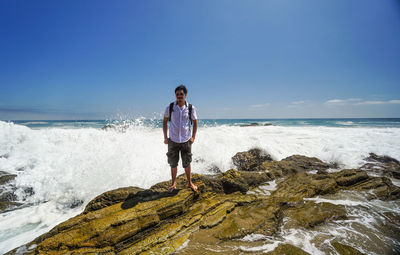 Man standing on rock by sea against clear sky