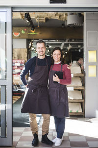 Full length portrait of confident smiling owners wearing aprons while standing in store