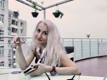 Portrait of mature woman smoking cigarette while using phone at table in terrace