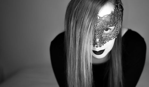 Close-up portrait of young woman wearing mask while standing against wall