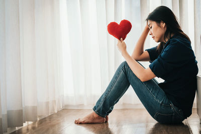 Side view of woman holding heart shape sitting at home