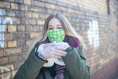 Portrait of young woman wearing mask against wall