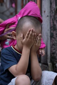 Boy covering face with hands while sitting outdoors