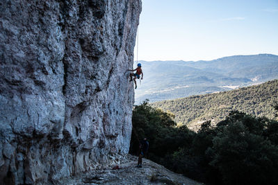 Man climbing on rock formation against sky