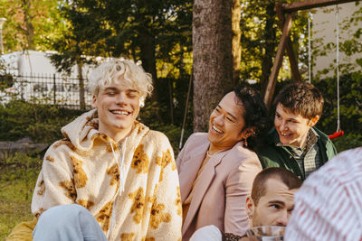 Gay friends laughing while sitting next to each other during dinner party in back yard