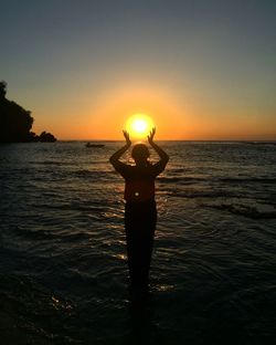 Man standing in sea against sky during sunset