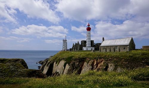 Lighthouse amidst sea and buildings against sky