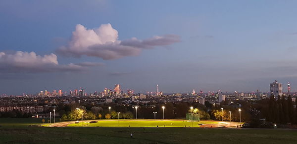 Illuminated buildings in city against cloudy sky