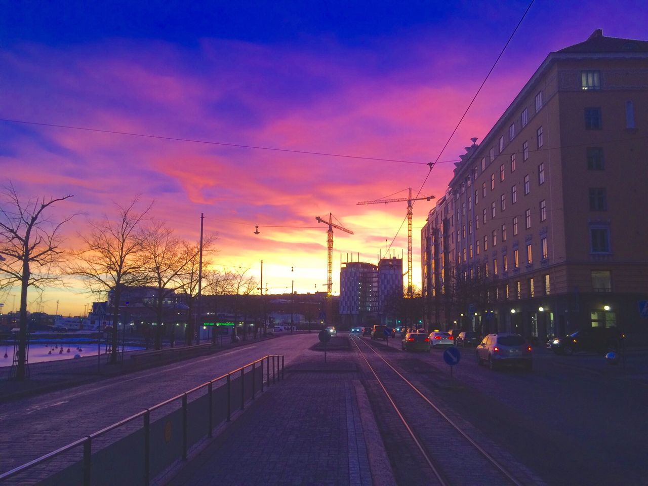 sunset, building exterior, architecture, built structure, city, transportation, sky, the way forward, cloud - sky, car, street light, street, diminishing perspective, road, city life, dusk, orange color, mode of transport, land vehicle, vanishing point