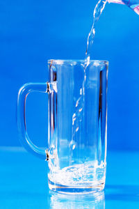 Close-up of water pouring in glass against blue background