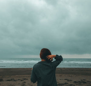 Rear view of woman standing at beach against cloudy sky