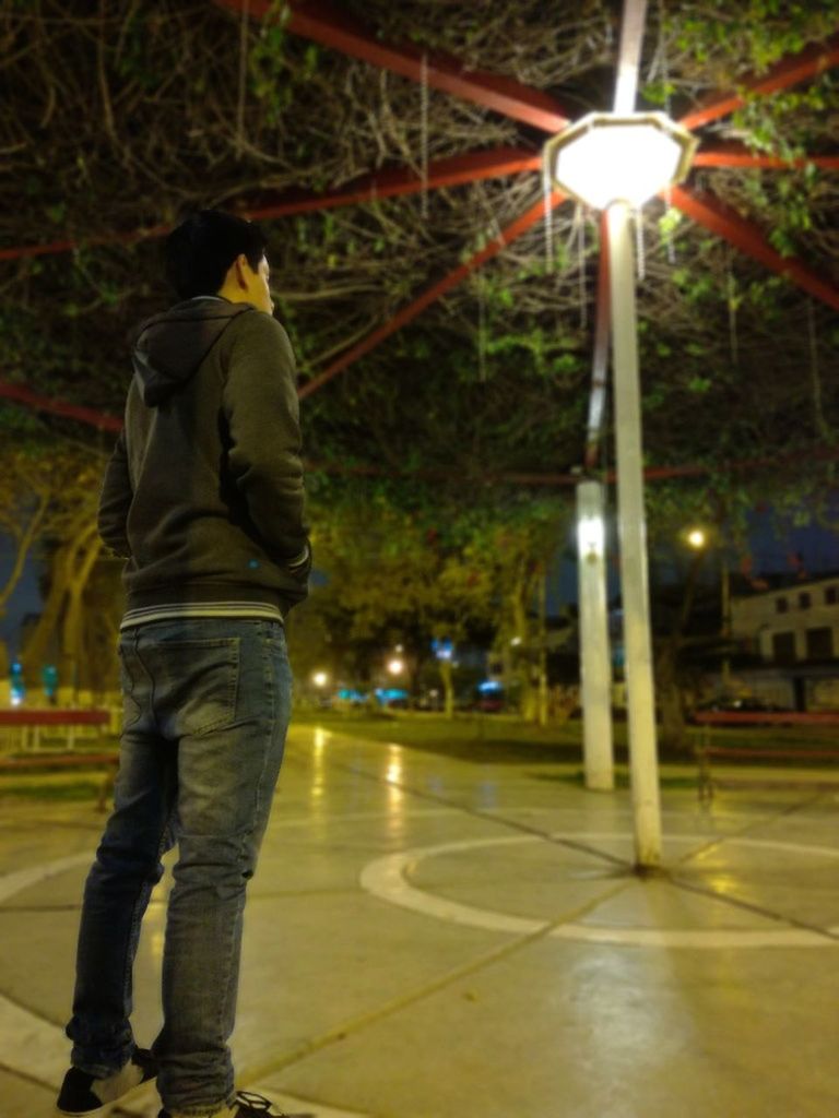 REAR VIEW OF MAN STANDING BY ILLUMINATED STREET LIGHT