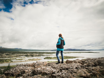 Rear view of woman standing on rock by sea against sky