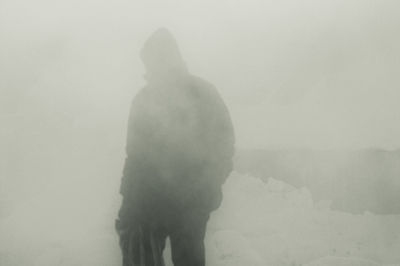 Rear view of man walking on snow covered landscape in foggy weather