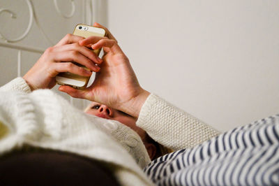 Close-up of woman with cellphone relaxing on bed