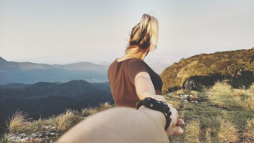 Cropped hand of man holding woman standing at mountain peak against sky