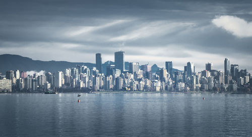 Sea by modern buildings against sky in city