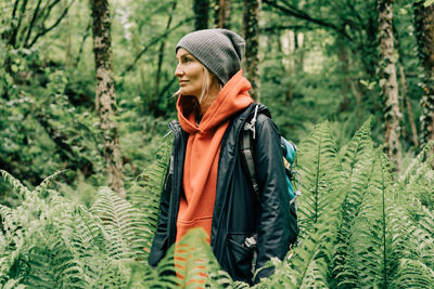 Woman hiker with a backpack in thickets of ferns in the spring forest