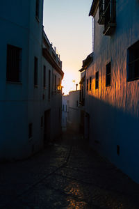 Narrow street amidst buildings against sky during sunset