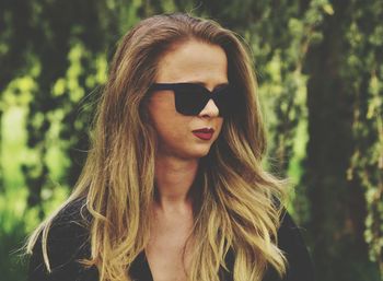 Close-up of mid adult woman wearing sunglasses against tree