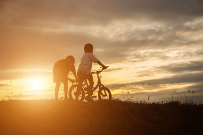 Silhouette man riding bicycle on field against sky during sunset