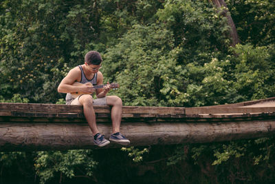 Young man playing ukulele on footbridge