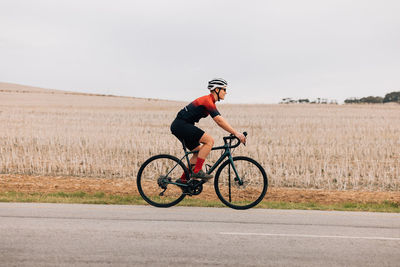 Side view woman riding bicycle on road against field