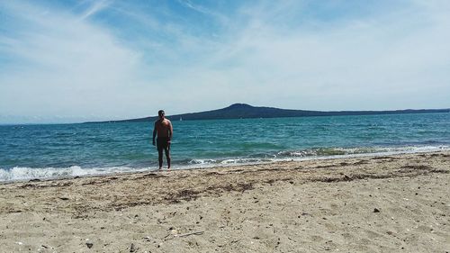 Full length of shirtless man standing at beach during sunny day