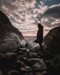 Man standing on rocks against sky during sunset