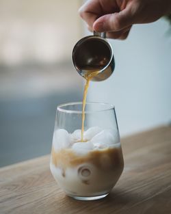 Close-up of hand pouring drink in glass on table