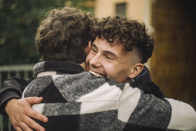 Happy boy with curly hair embracing male friend wearing flannel shirt