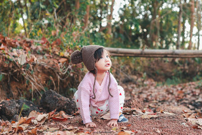 Cute baby girl looking away while crouching on land during winter