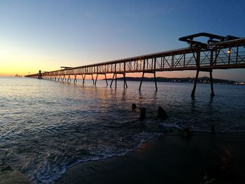 Silhouette bridge over sea against clear sky during sunset