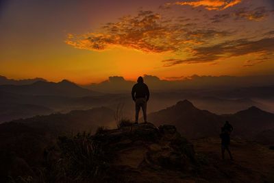 Rear view of silhouette man standing on mountain against sky during sunrise
