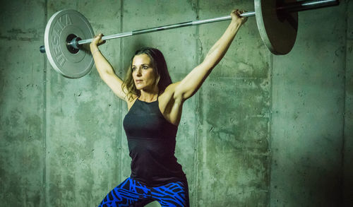 Beautiful woman lifting barbell against wall