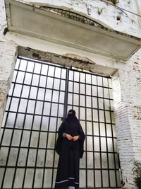 Woman wearing black hijab standing against gate