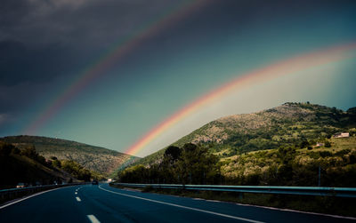 Rainbow over road against sky