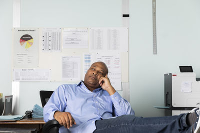 Thoughtful mature employee looking away while sitting in print shop