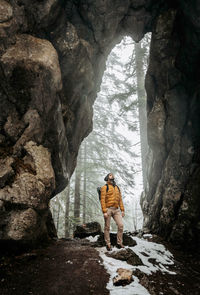 Front view of man standing in front of natural doorway in rock. winter, snow, hiking, exploring.