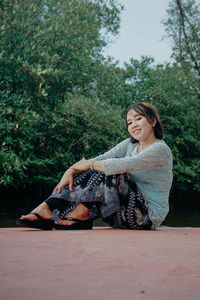 Young woman looking away while sitting on tree