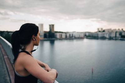 Side view of female athlete looking at city while standing on footbridge over sea