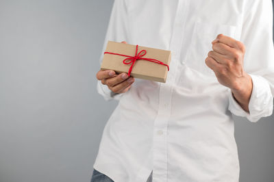 Midsection of man holding paper while standing against white background