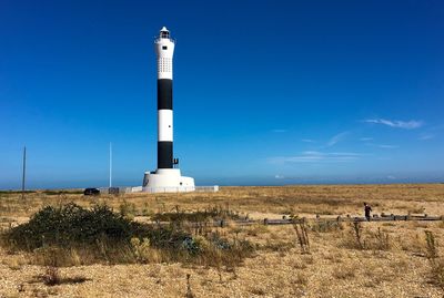 Lighthouse on field against blue sky