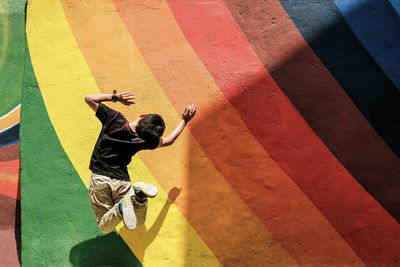 Rear view of boy jumping against rainbow wall