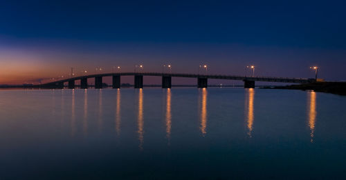 Illuminated bridge over sea against sky at dusk