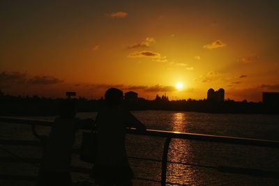 Silhouette people standing by sea against sky during sunset